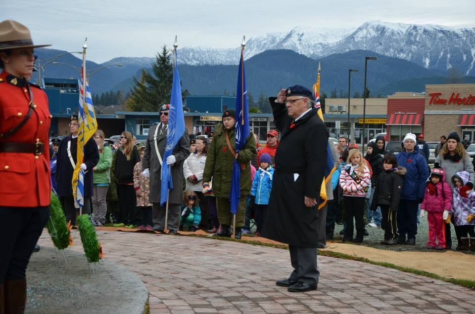 A Veteran salutes at the Kitimat cenotaph with the colour party behind